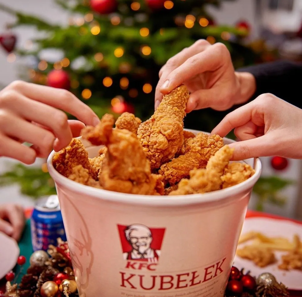 Dłonie sięgające po kurczaka z kubełka KFC przy świątecznym stole