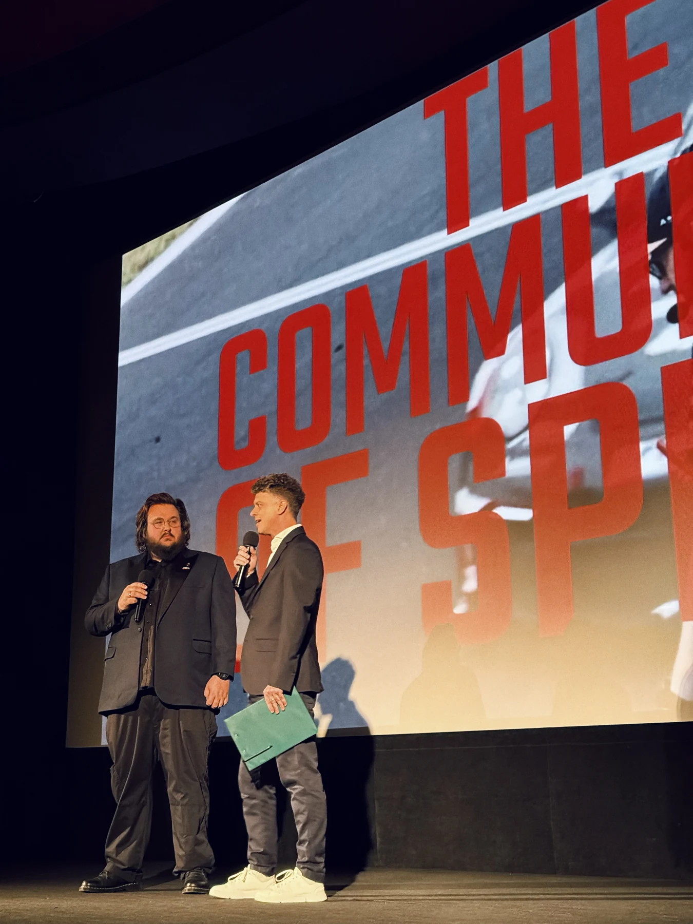 Dwie osoby z mikrofonami przed ekranem z tytułem The Community of Speed